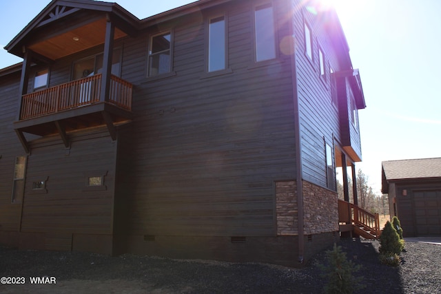 view of home's exterior featuring stone siding, crawl space, a balcony, and a garage