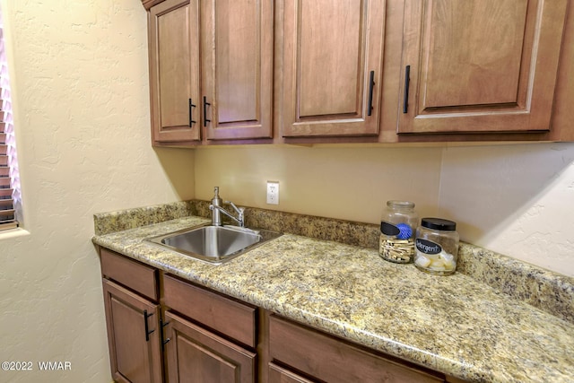 kitchen featuring light stone countertops, brown cabinets, a sink, and a textured wall