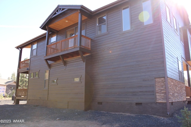 view of side of home with stone siding, crawl space, and a balcony