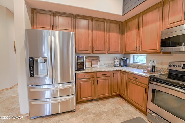 kitchen featuring light tile patterned floors, stainless steel appliances, brown cabinets, and light stone countertops