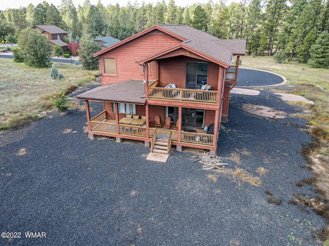 rustic home with roof with shingles, driveway, a deck, and a forest view