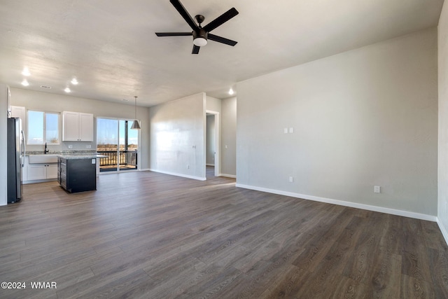 unfurnished living room featuring dark wood-style flooring, baseboards, ceiling fan, and a sink