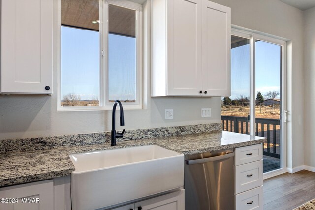 kitchen with light stone countertops, stainless steel dishwasher, white cabinetry, and a sink