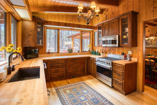 kitchen with a sink, appliances with stainless steel finishes, wooden counters, wooden walls, and a notable chandelier