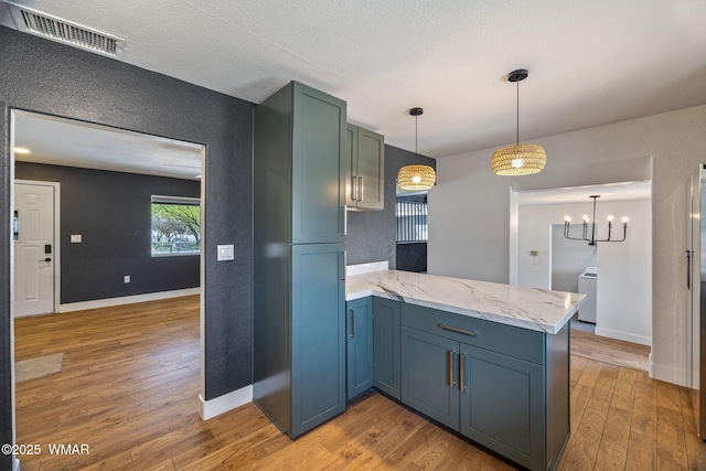 kitchen with visible vents, a textured wall, a peninsula, and light wood finished floors