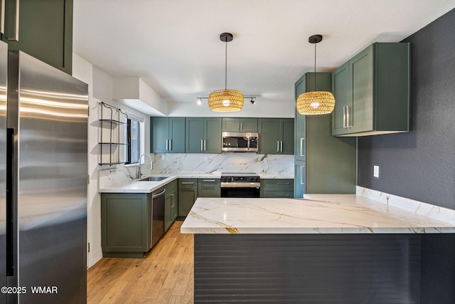 kitchen featuring a sink, appliances with stainless steel finishes, green cabinetry, and a peninsula