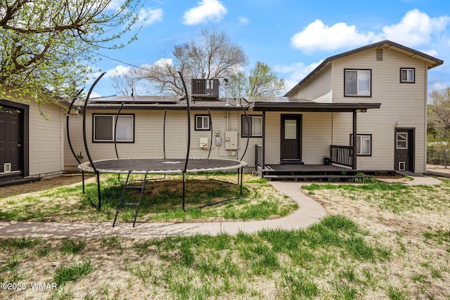 rear view of house featuring a trampoline, central AC, a porch, solar panels, and a yard
