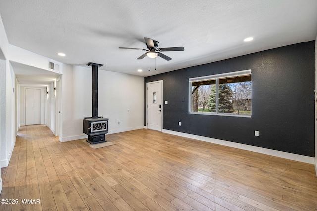 spare room featuring visible vents, a wood stove, light wood finished floors, and a ceiling fan