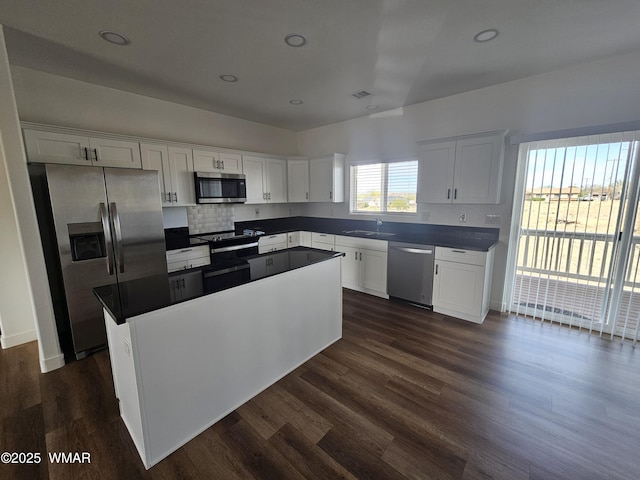kitchen featuring a kitchen island, backsplash, white cabinets, stainless steel appliances, and dark wood-type flooring