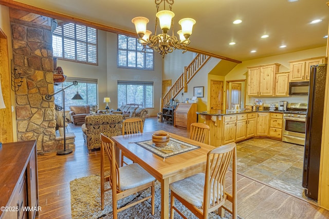 dining room with a notable chandelier, recessed lighting, a towering ceiling, light wood-style floors, and stairs