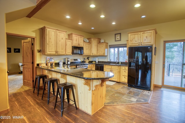 kitchen with a sink, black appliances, dark stone countertops, a peninsula, and a kitchen bar