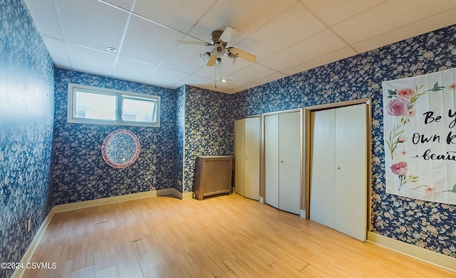 empty room with a drop ceiling, ceiling fan, and light wood-type flooring