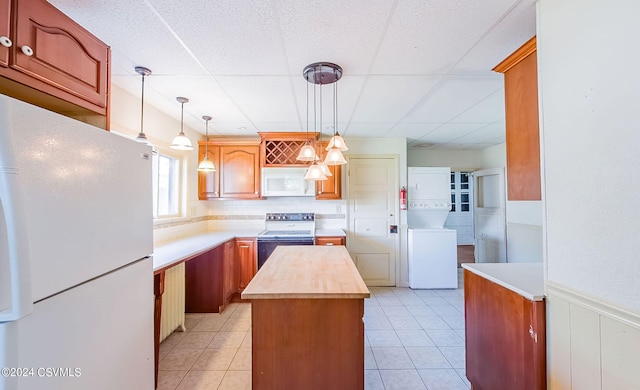 kitchen featuring white appliances, stacked washing maching and dryer, a center island, decorative light fixtures, and butcher block counters