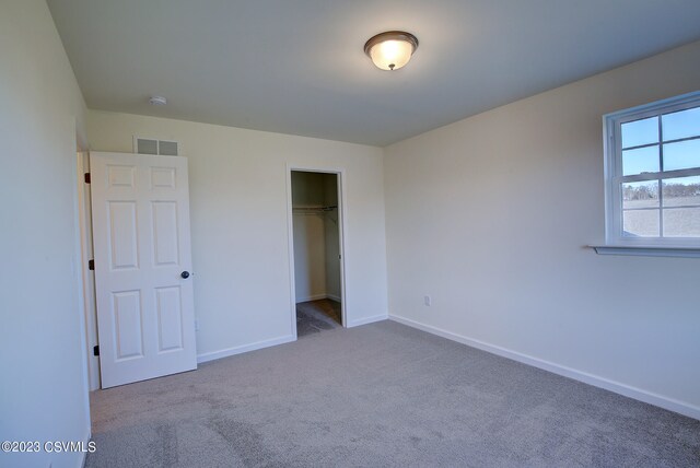 unfurnished bedroom featuring a spacious closet, a closet, and dark colored carpet