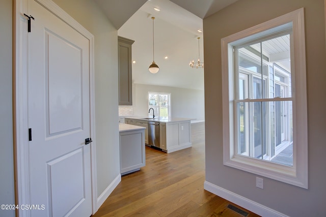 kitchen featuring sink, dishwasher, kitchen peninsula, hanging light fixtures, and light hardwood / wood-style floors