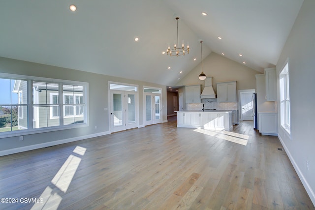 unfurnished living room featuring a notable chandelier, high vaulted ceiling, sink, and light wood-type flooring