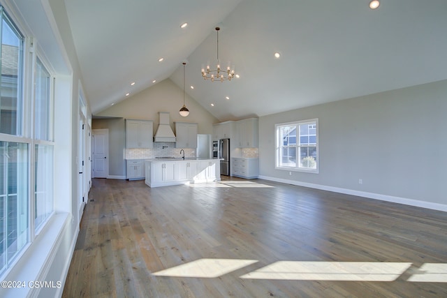 unfurnished living room with a notable chandelier, high vaulted ceiling, sink, and light wood-type flooring