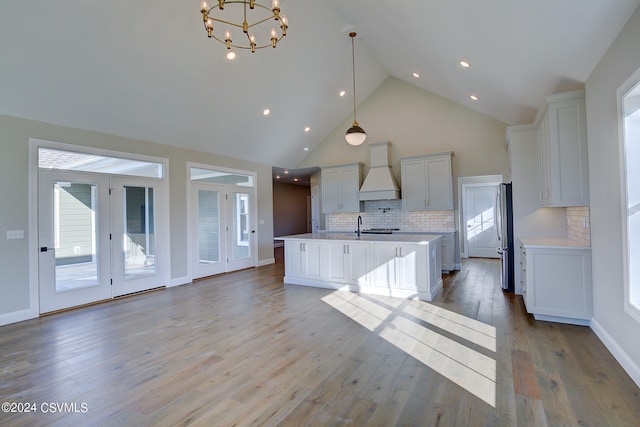 kitchen with light wood-type flooring, hanging light fixtures, white cabinets, premium range hood, and a kitchen island with sink