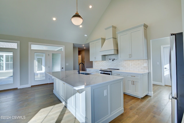 kitchen with hanging light fixtures, high vaulted ceiling, custom range hood, sink, and stainless steel appliances