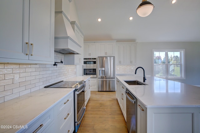 kitchen with custom range hood, a center island with sink, sink, white cabinets, and appliances with stainless steel finishes