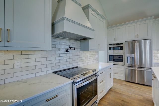 kitchen featuring decorative backsplash, light hardwood / wood-style flooring, white cabinetry, custom exhaust hood, and appliances with stainless steel finishes