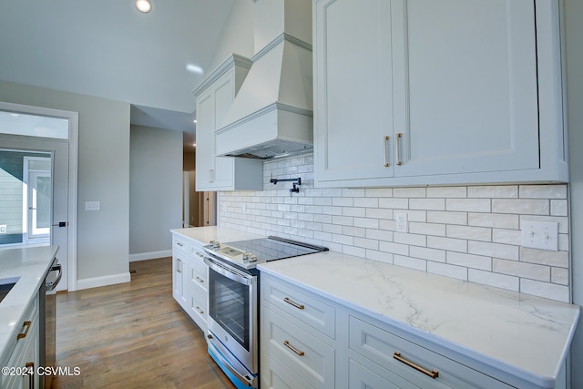 kitchen featuring appliances with stainless steel finishes, light stone countertops, light wood-type flooring, white cabinetry, and custom exhaust hood