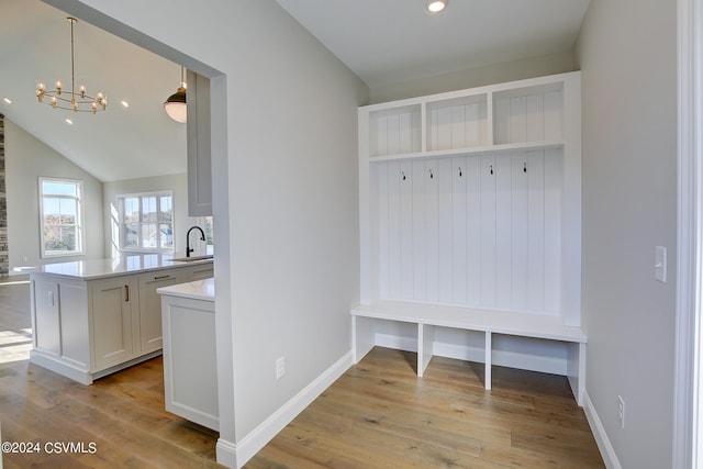 mudroom with sink, light hardwood / wood-style floors, a notable chandelier, and vaulted ceiling