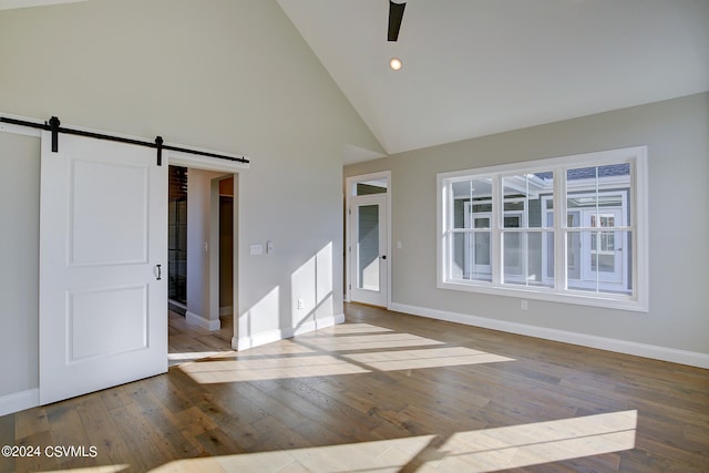 unfurnished room with hardwood / wood-style floors, a barn door, and high vaulted ceiling