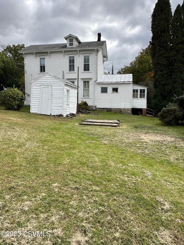 rear view of property with a lawn and a storage unit