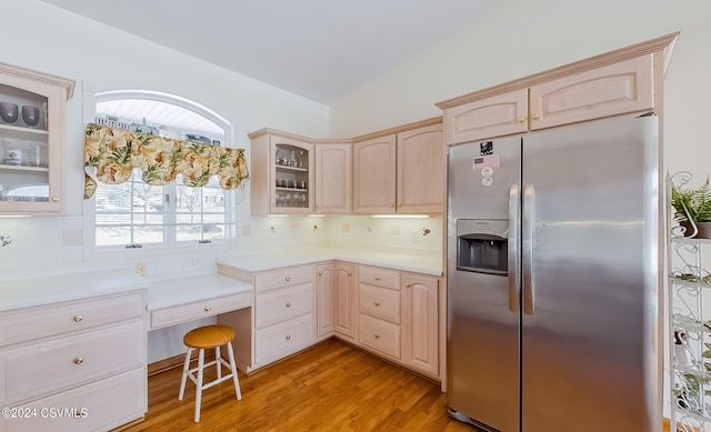 kitchen with stainless steel refrigerator with ice dispenser, vaulted ceiling, light wood-type flooring, light brown cabinets, and backsplash