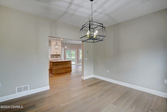 unfurnished dining area with a notable chandelier and wood-type flooring