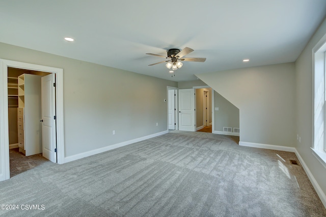 unfurnished bedroom featuring light colored carpet, a closet, a spacious closet, and ceiling fan