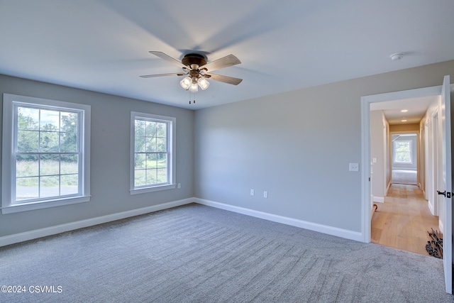 spare room featuring ceiling fan, a wealth of natural light, and light carpet