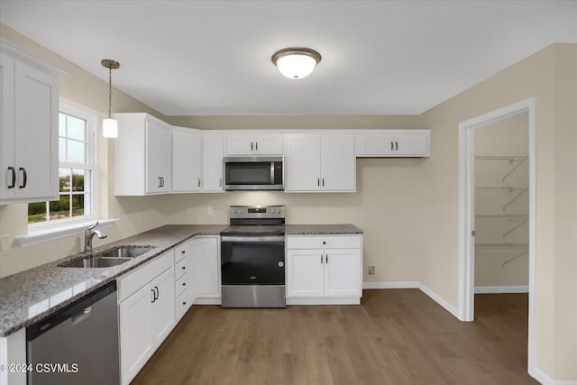 kitchen with white cabinets, appliances with stainless steel finishes, hanging light fixtures, and dark wood-type flooring