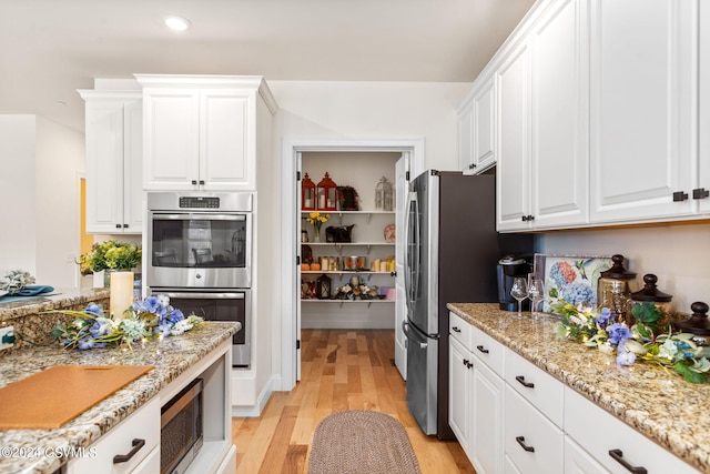 kitchen featuring white cabinets, light hardwood / wood-style flooring, appliances with stainless steel finishes, and light stone counters