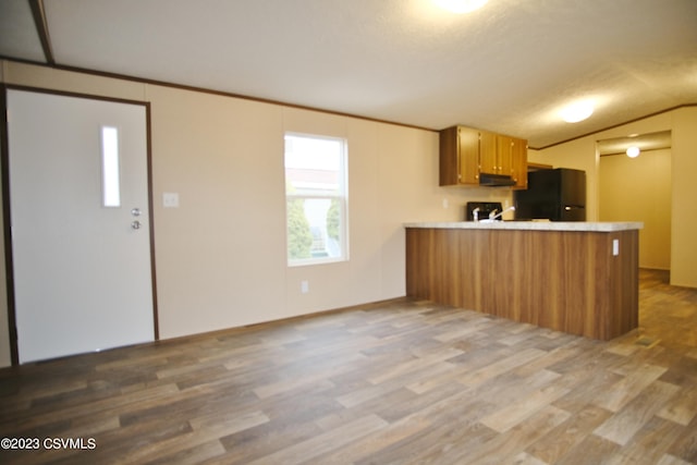 kitchen featuring black refrigerator, kitchen peninsula, lofted ceiling, extractor fan, and hardwood / wood-style flooring