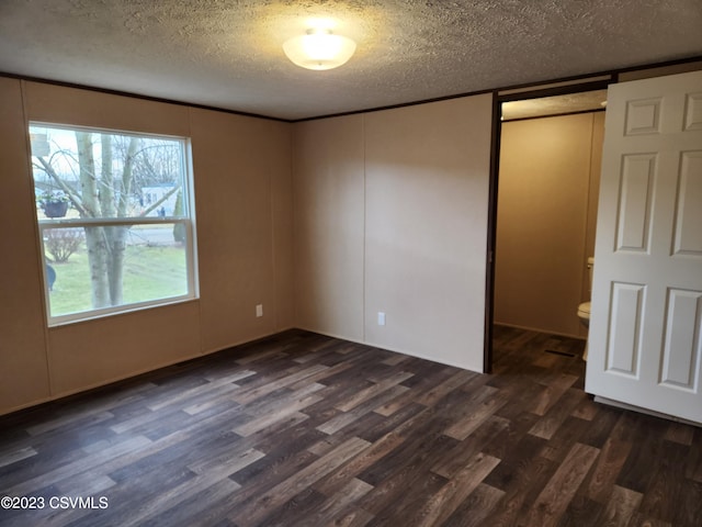 unfurnished bedroom featuring a barn door, a textured ceiling, connected bathroom, and dark hardwood / wood-style floors