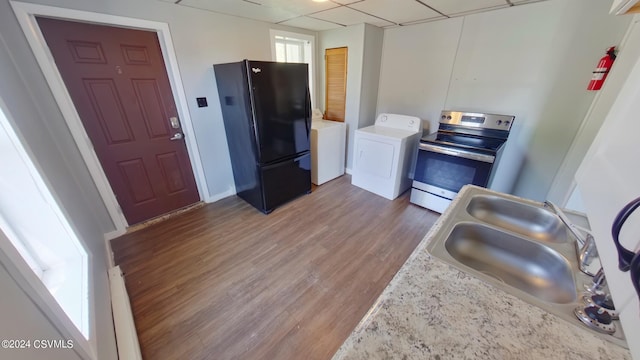 kitchen featuring stainless steel range with electric cooktop, washer / clothes dryer, black fridge, and hardwood / wood-style floors