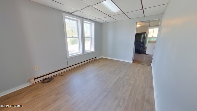 empty room with a wealth of natural light, light hardwood / wood-style flooring, a drop ceiling, and a baseboard radiator