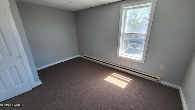 carpeted empty room featuring a drop ceiling, a baseboard radiator, and a wealth of natural light