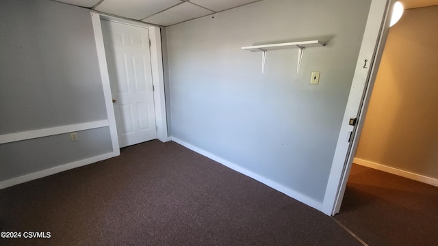 empty room with a drop ceiling and dark colored carpet