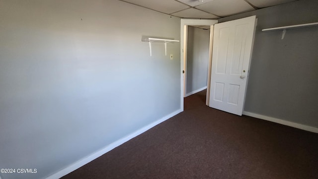 unfurnished bedroom featuring a drop ceiling and dark carpet