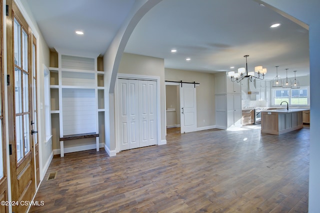 unfurnished living room featuring sink, a barn door, dark hardwood / wood-style floors, and a chandelier