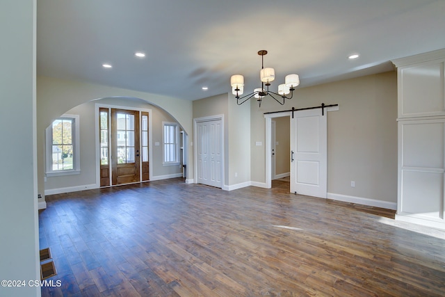 spare room with a barn door, a notable chandelier, and dark hardwood / wood-style floors