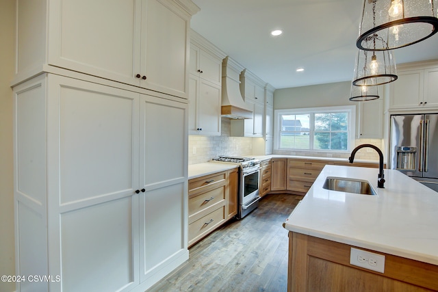 kitchen featuring premium range hood, light hardwood / wood-style flooring, pendant lighting, sink, and premium appliances