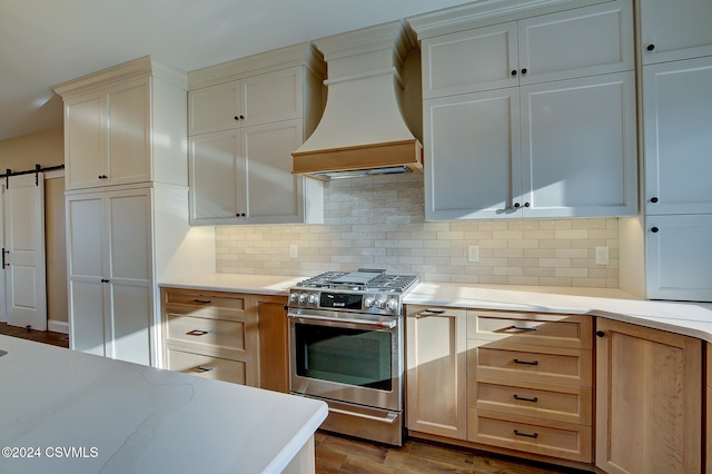 kitchen with light hardwood / wood-style flooring, backsplash, high end stainless steel range oven, a barn door, and premium range hood