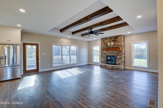 unfurnished living room with dark wood-type flooring, a stone fireplace, beamed ceiling, and plenty of natural light