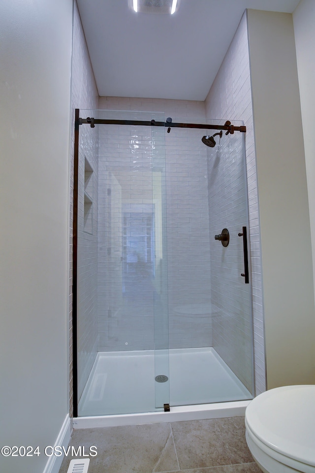 bathroom featuring toilet, a shower with shower door, and tile patterned flooring