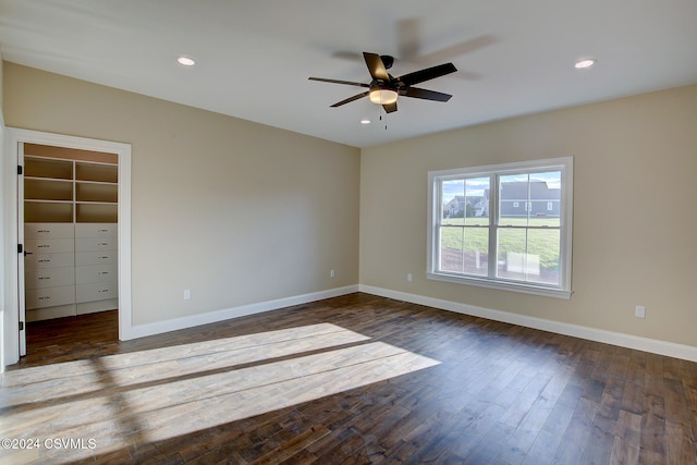 unfurnished bedroom with a walk in closet, a closet, dark wood-type flooring, and ceiling fan