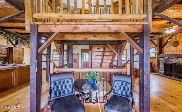 sitting room with beamed ceiling, light hardwood / wood-style floors, a stone fireplace, and wood ceiling